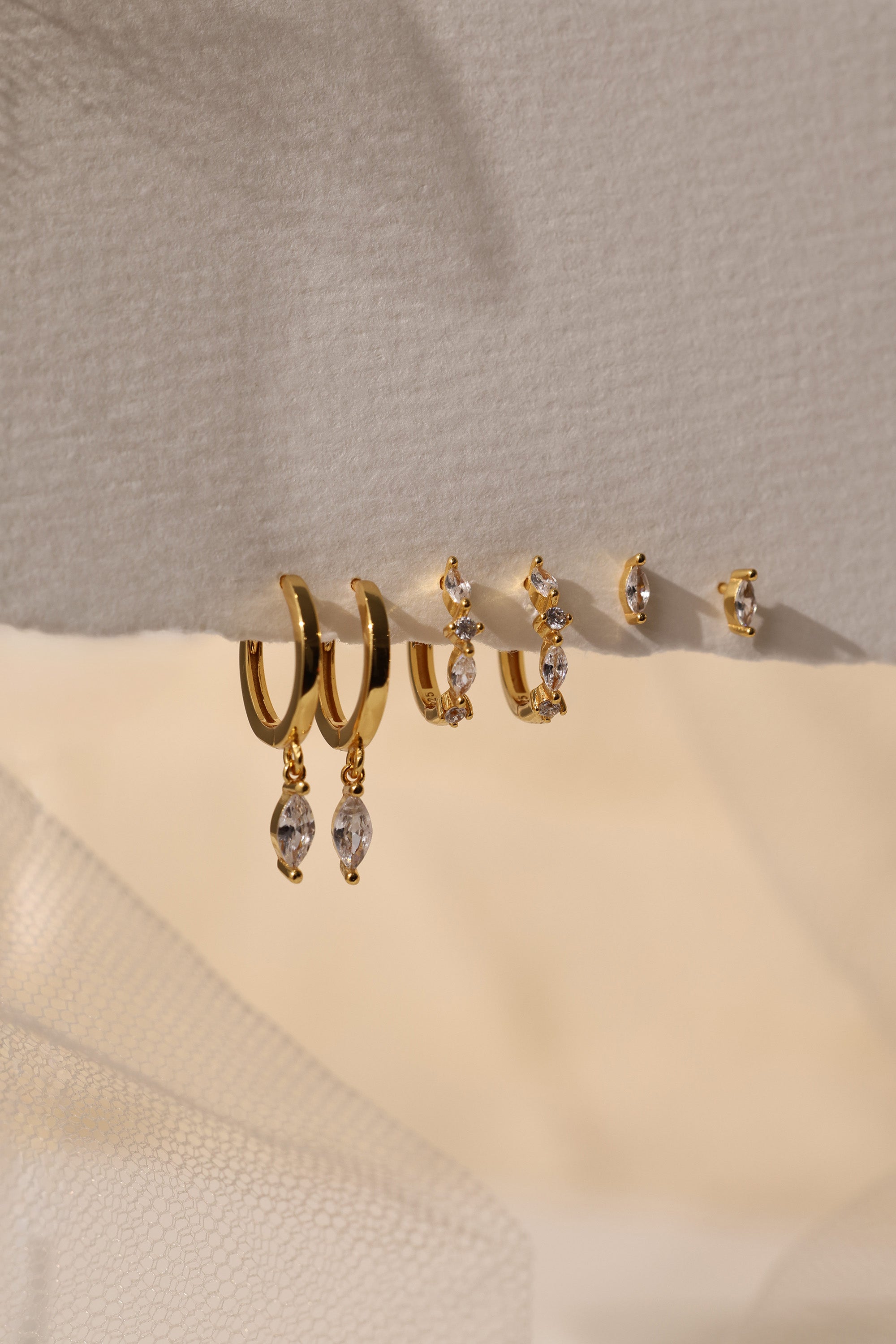 Grace Dangle GOLD Earring Set in 18K gold‑plated sterling silver with marquise‑cut cubic zirconia, elegant hoop design on beige surface