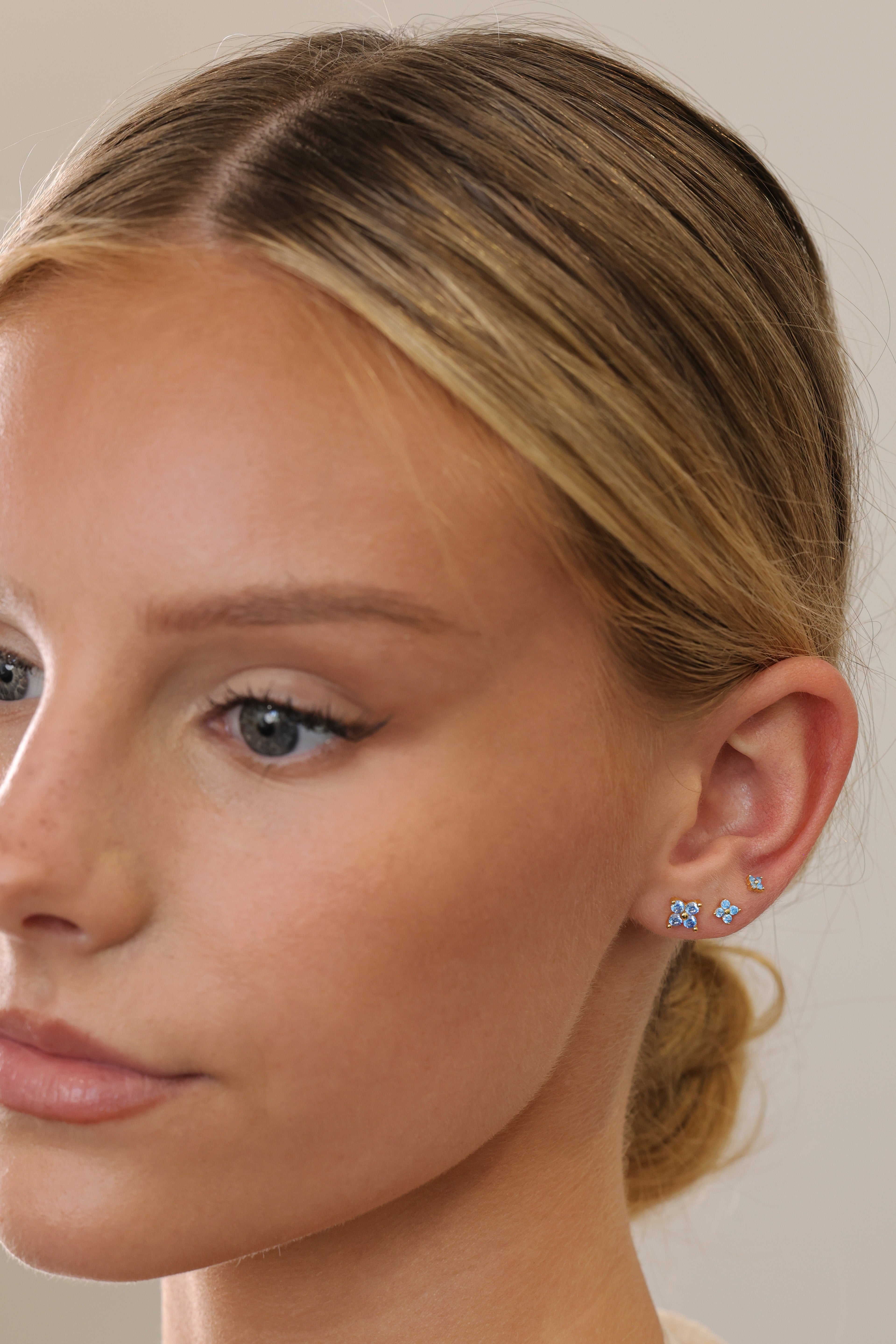 Gold 4 clover blue stud earrings worn in 6mm, 4mm and 3mm on a model's ear, three-quarter view