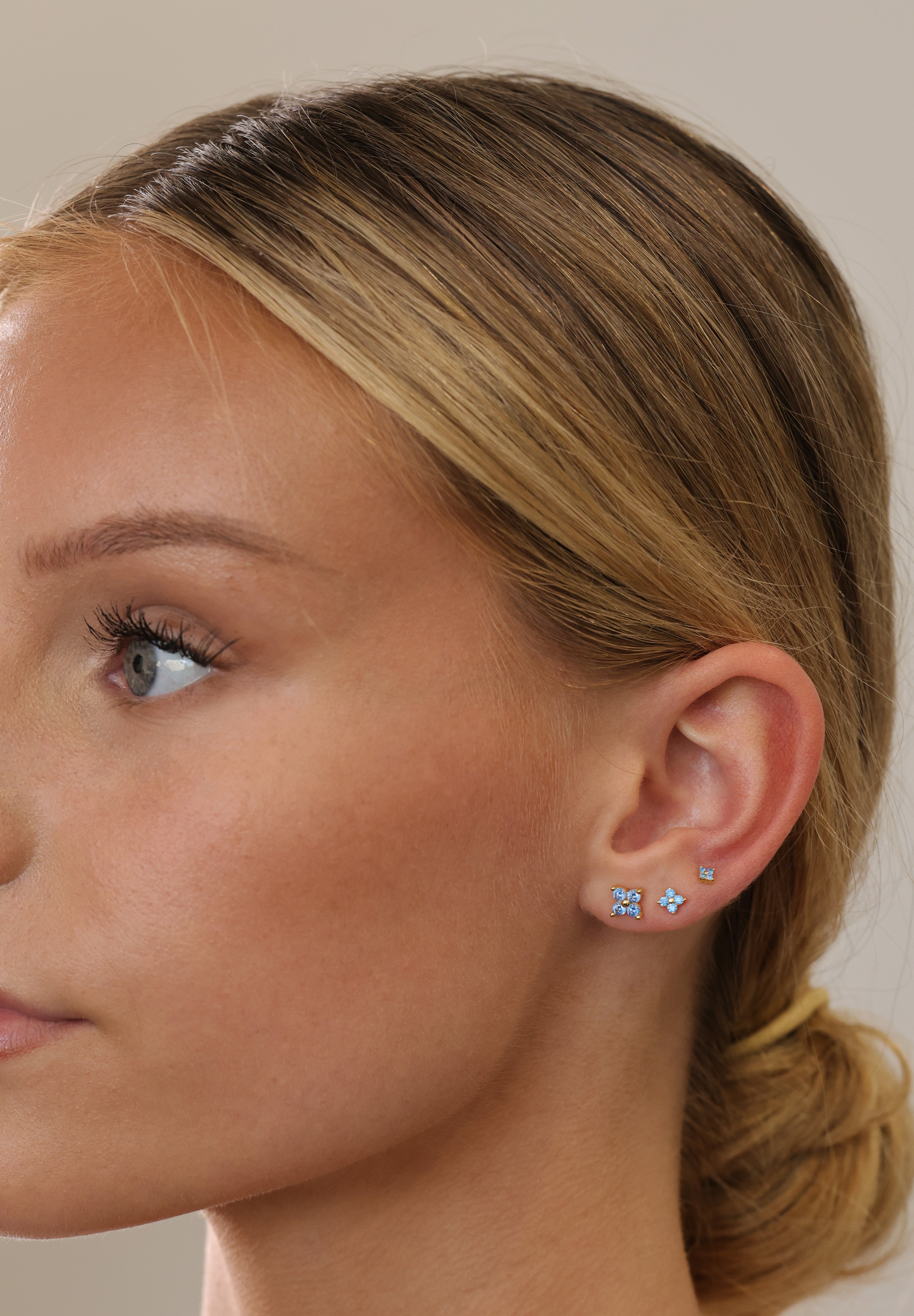 Model wearing gold 4 clover blue stud earrings stacked in three sizes on one ear, side profile