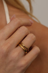 A close-up of a person's hand wearing two thin, polished gold rings stacked together.