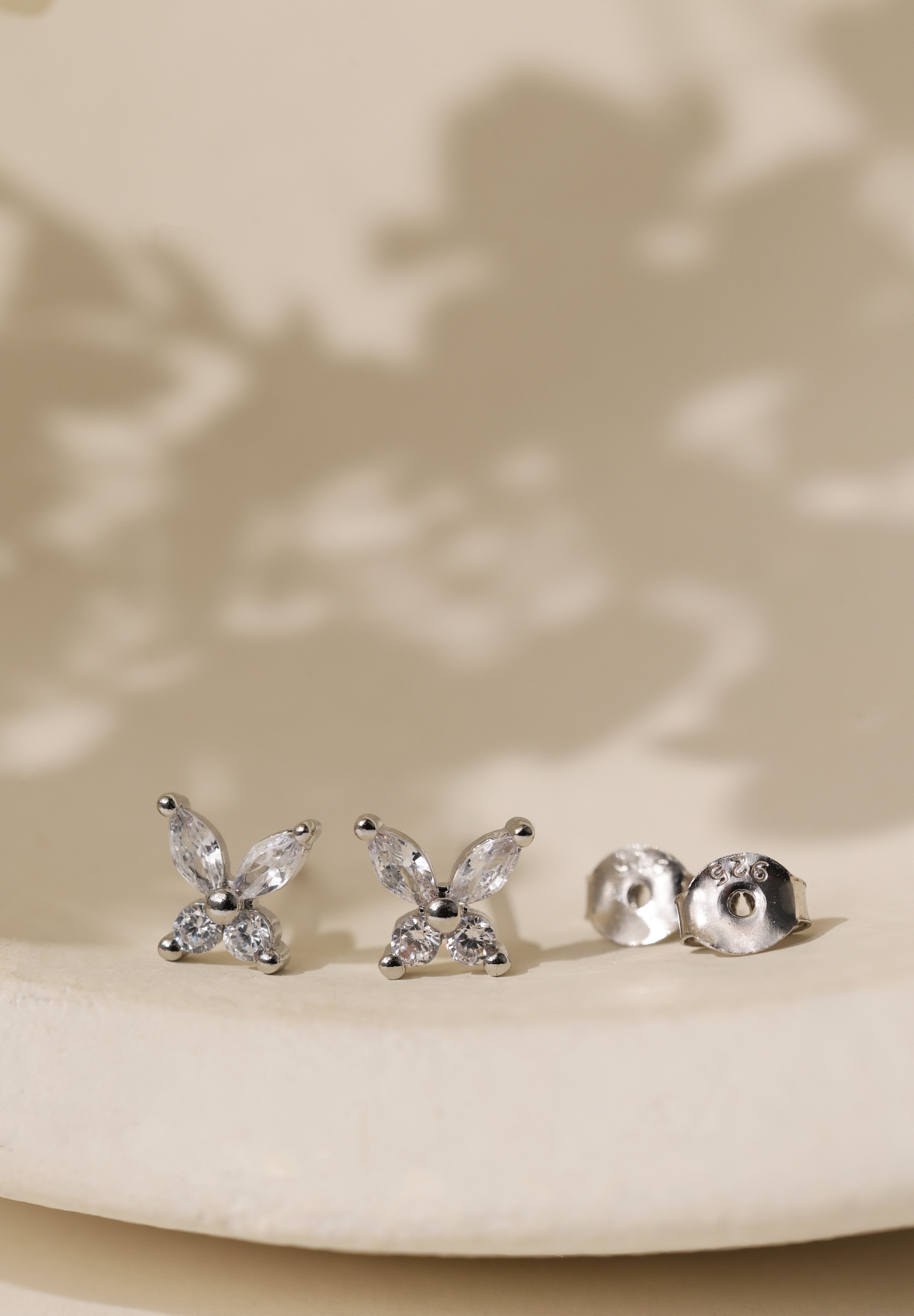 Sterling silver butterfly cubic zirconia stud earrings on a cream dish beside their 925 butterfly backs.