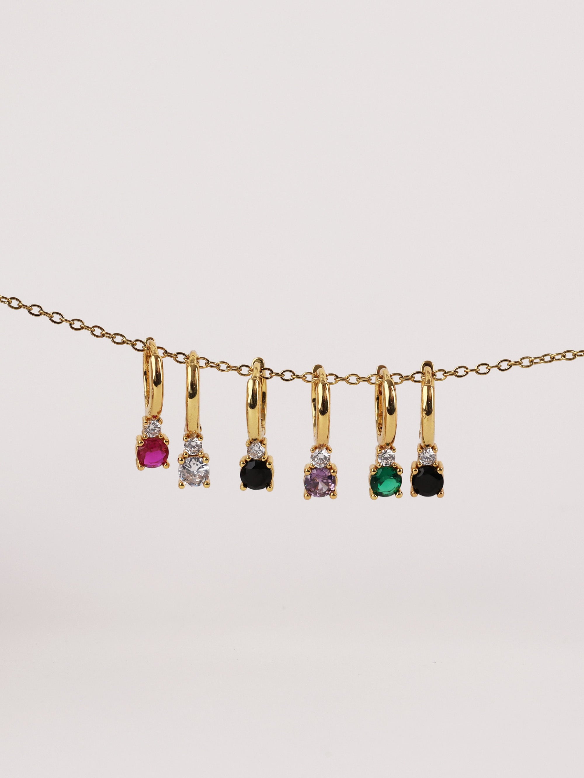 Gold hoop earrings with colorful gemstones in pink, clear, black, purple, green, and black.