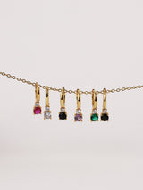 Gold hoop earrings with colorful gemstones in pink, clear, black, purple, green, and black.
