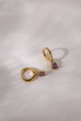 Gold hoop earrings with colorful gemstones in pink, clear, black, purple, green, and black.