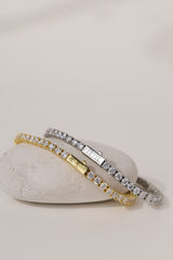 Gold 3mm cubic zirconia tennis bracelet draped over a white pebble, showing the engraved box clasp