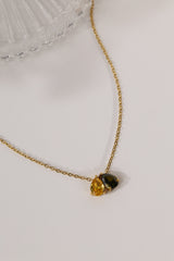 Gold birthstone necklace with two pear-cut stones on a fine cable chain, resting on a pale neutral background