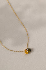 Gold birthstone necklace with two pear-cut stones on a fine cable chain, resting on a pale neutral background