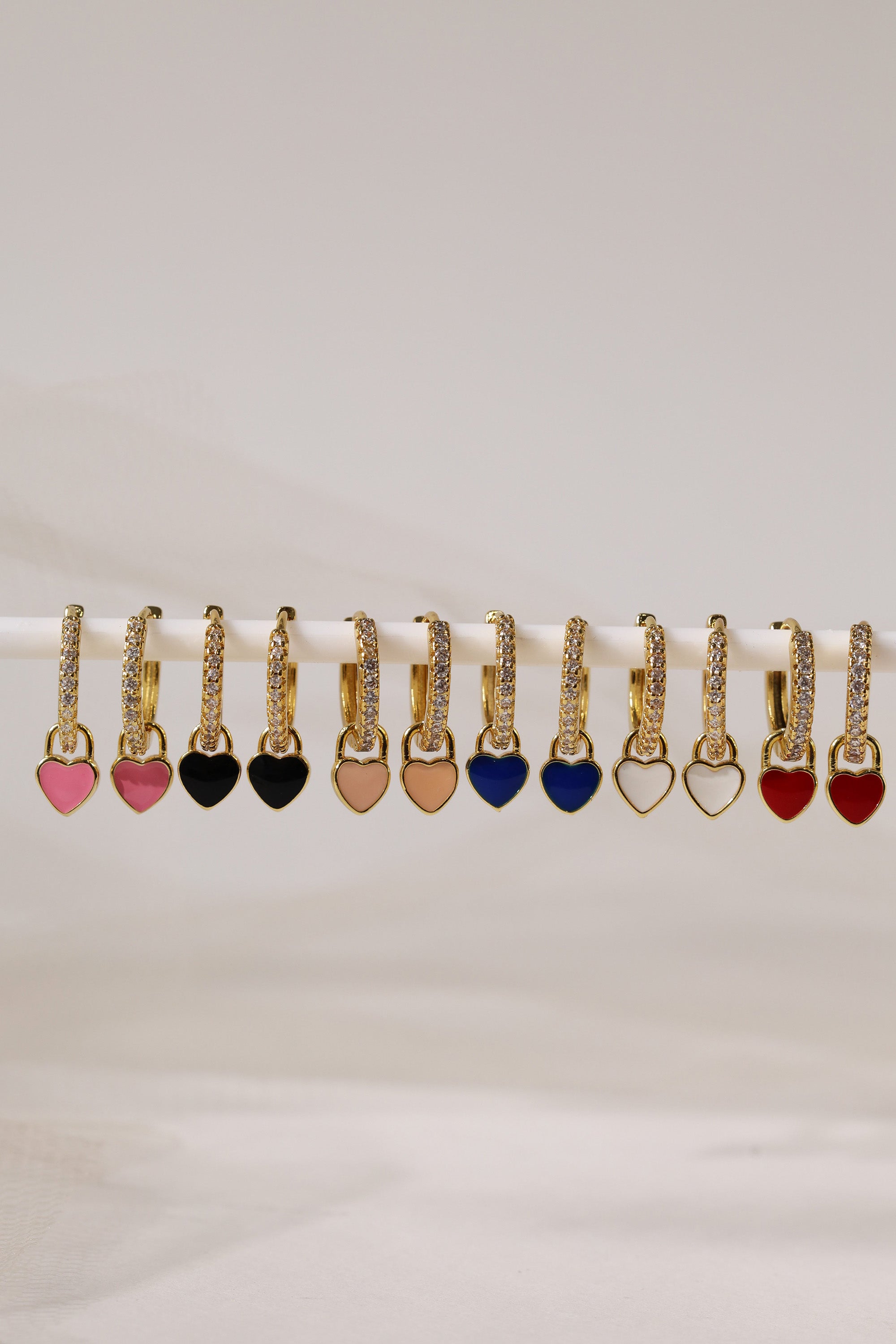 Dainty gold–plated hoop earrings with pave cubic zirconia and a removable heart charm, shown in four colour variations, available in gold and silver finishes.