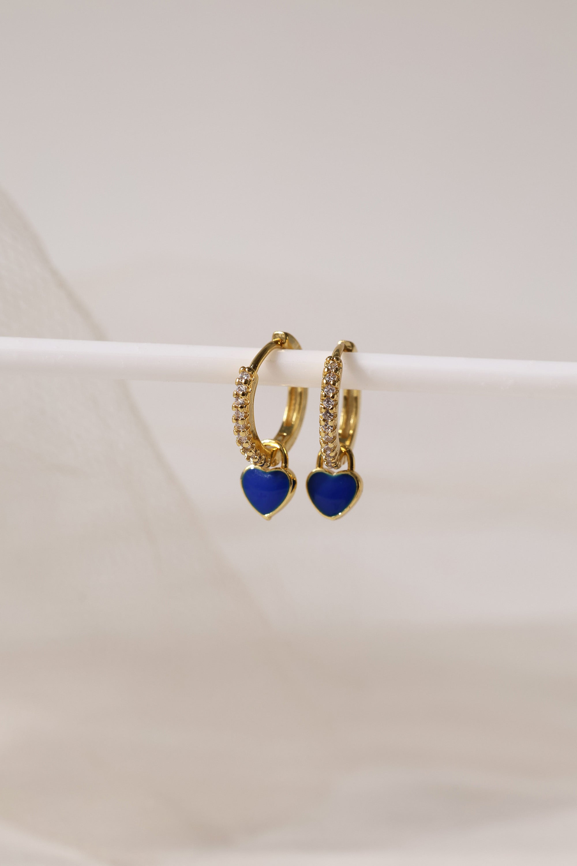 Dainty gold–plated hoop earrings with pave cubic zirconia and a removable heart charm, shown in four colour variations, available in gold and silver finishes.