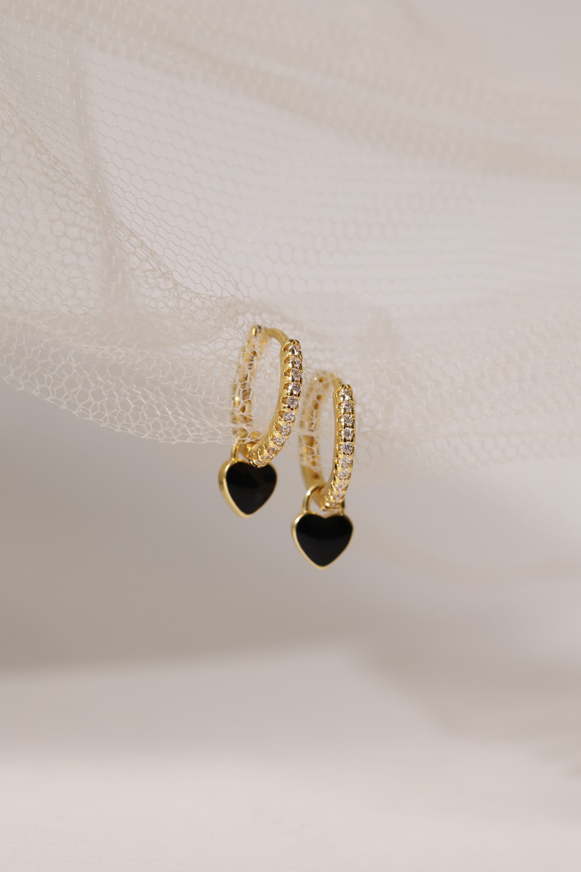 Dainty gold–plated hoop earrings with pave cubic zirconia and a removable heart charm, shown in four colour variations, available in gold and silver finishes.