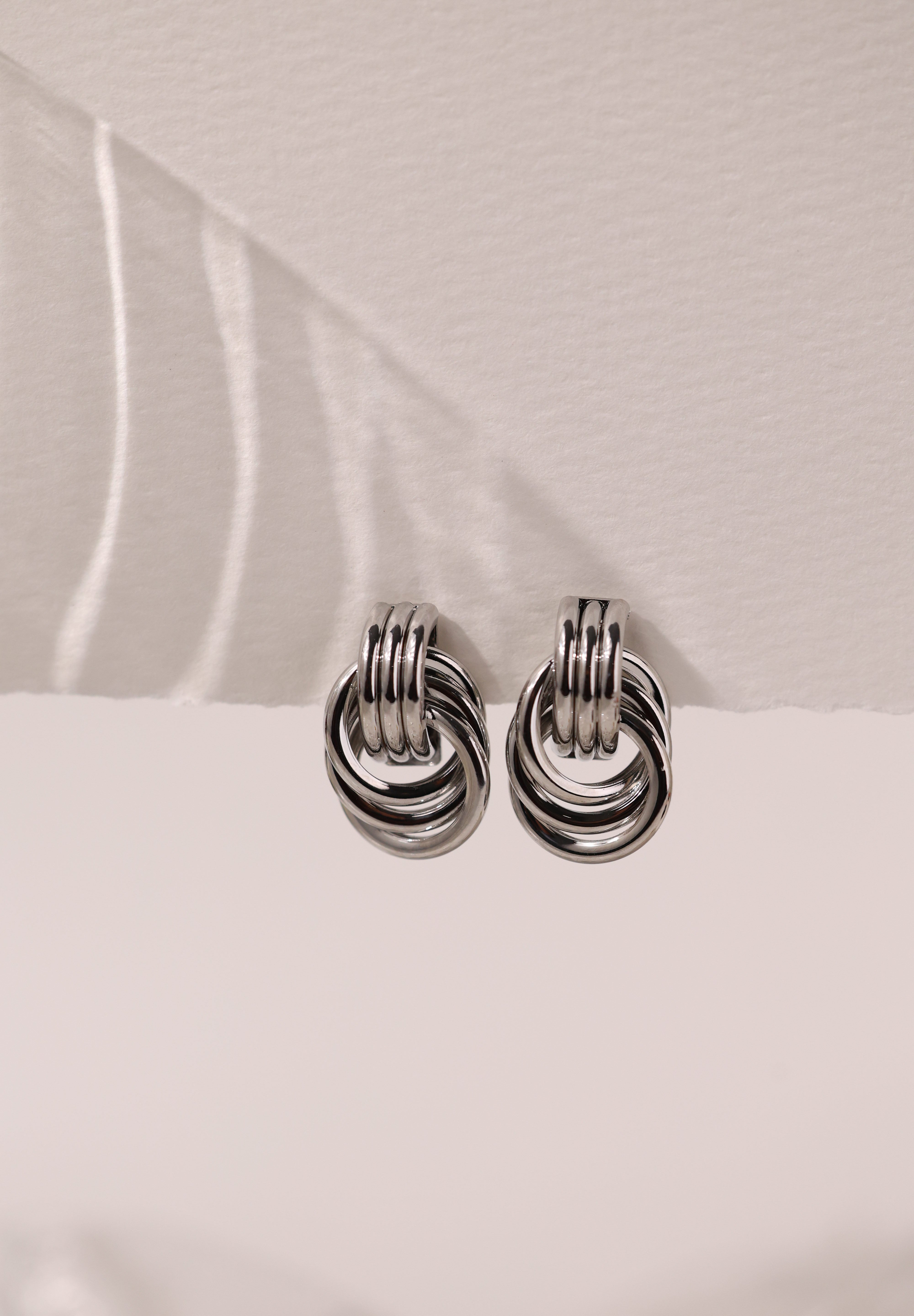 Silver interlocking ring earrings with a polished knot design that reflects light beautifully.