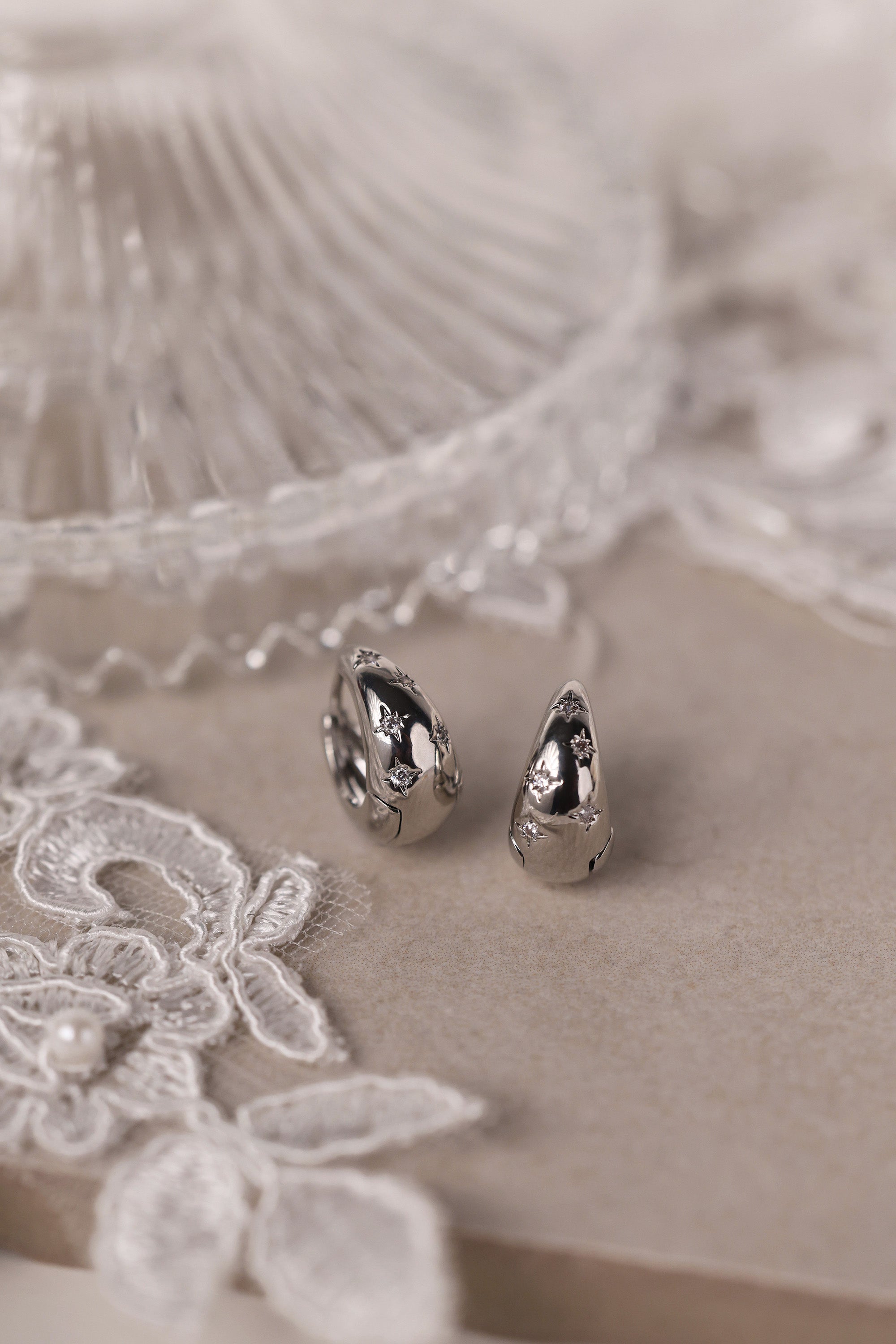 Gleaming silver hoop earrings with delicate star‑shaped engravings along the surface, reflecting light for a subtle sparkle; lightweight design shown in close‑up on a plain background.