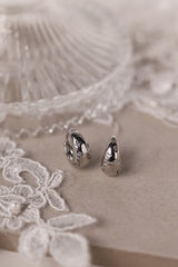 Gleaming silver hoop earrings with delicate star‑shaped engravings along the surface, reflecting light for a subtle sparkle; lightweight design shown in close‑up on a plain background.