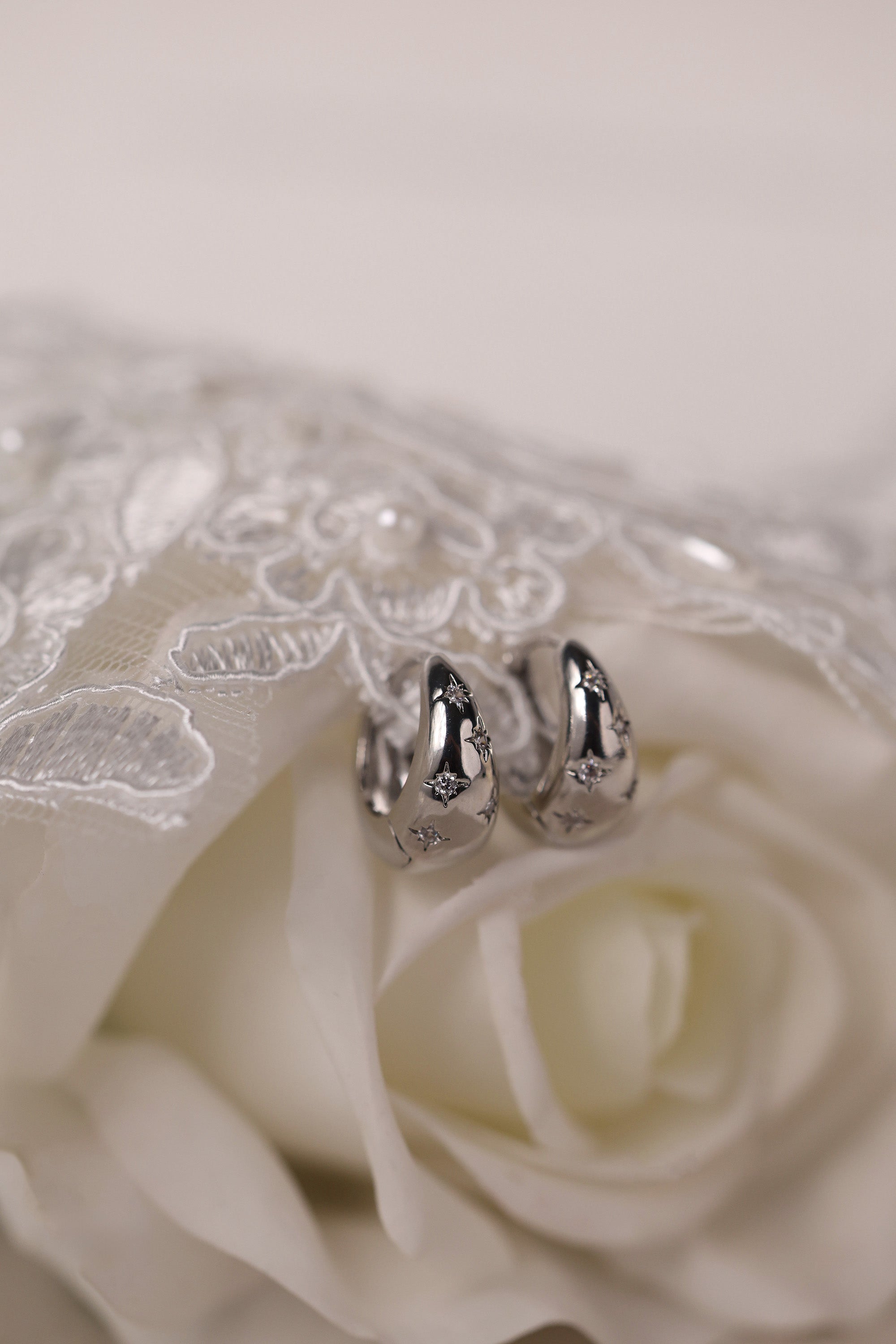 Gleaming silver hoop earrings with delicate star‑shaped engravings along the surface, reflecting light for a subtle sparkle; lightweight design shown in close‑up on a plain background.