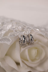 Gleaming silver hoop earrings with delicate star‑shaped engravings along the surface, reflecting light for a subtle sparkle; lightweight design shown in close‑up on a plain background.