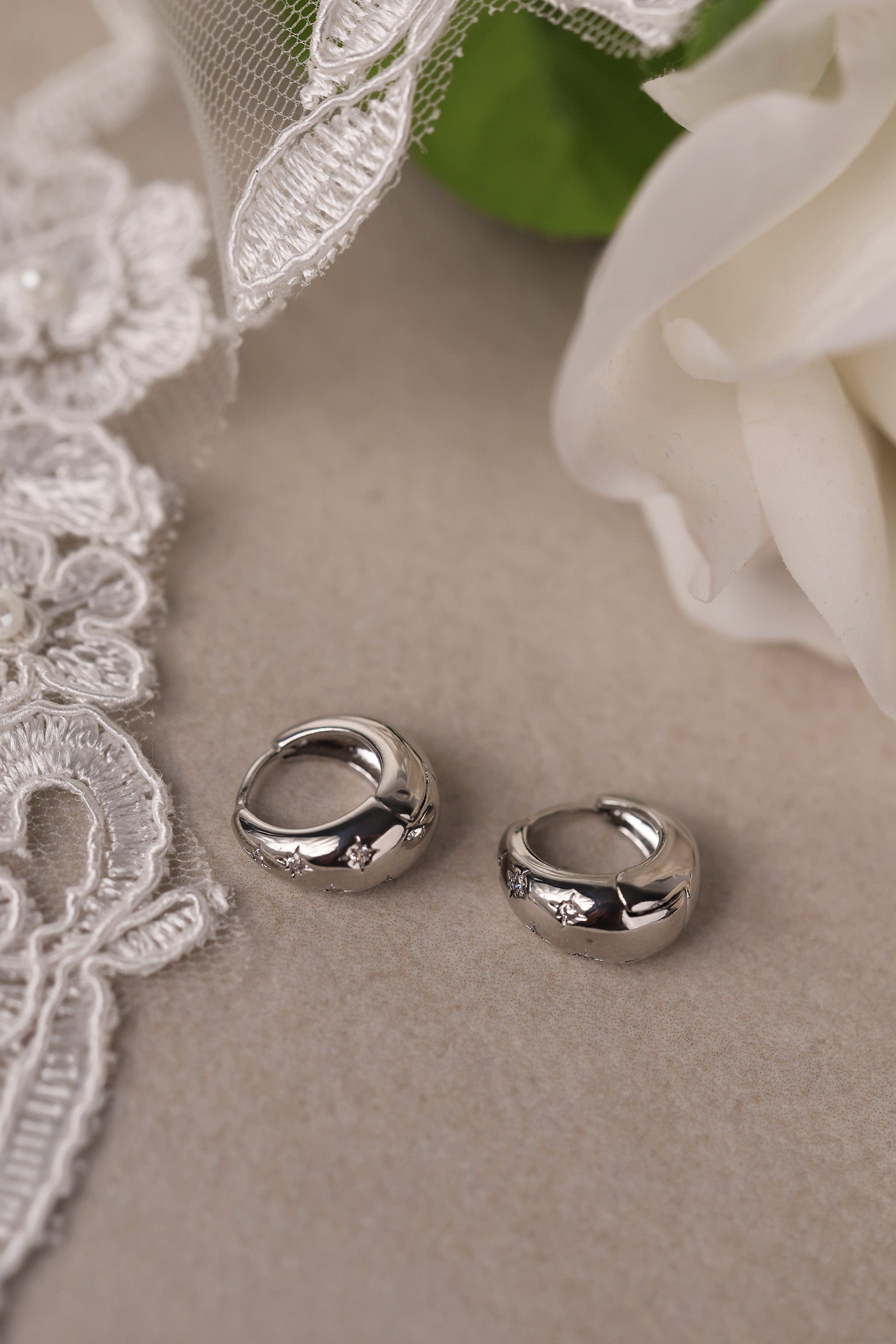 Gleaming silver hoop earrings with delicate star‑shaped engravings along the surface, reflecting light for a subtle sparkle; lightweight design shown in close‑up on a plain background.