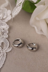 Gleaming silver hoop earrings with delicate star‑shaped engravings along the surface, reflecting light for a subtle sparkle; lightweight design shown in close‑up on a plain background.