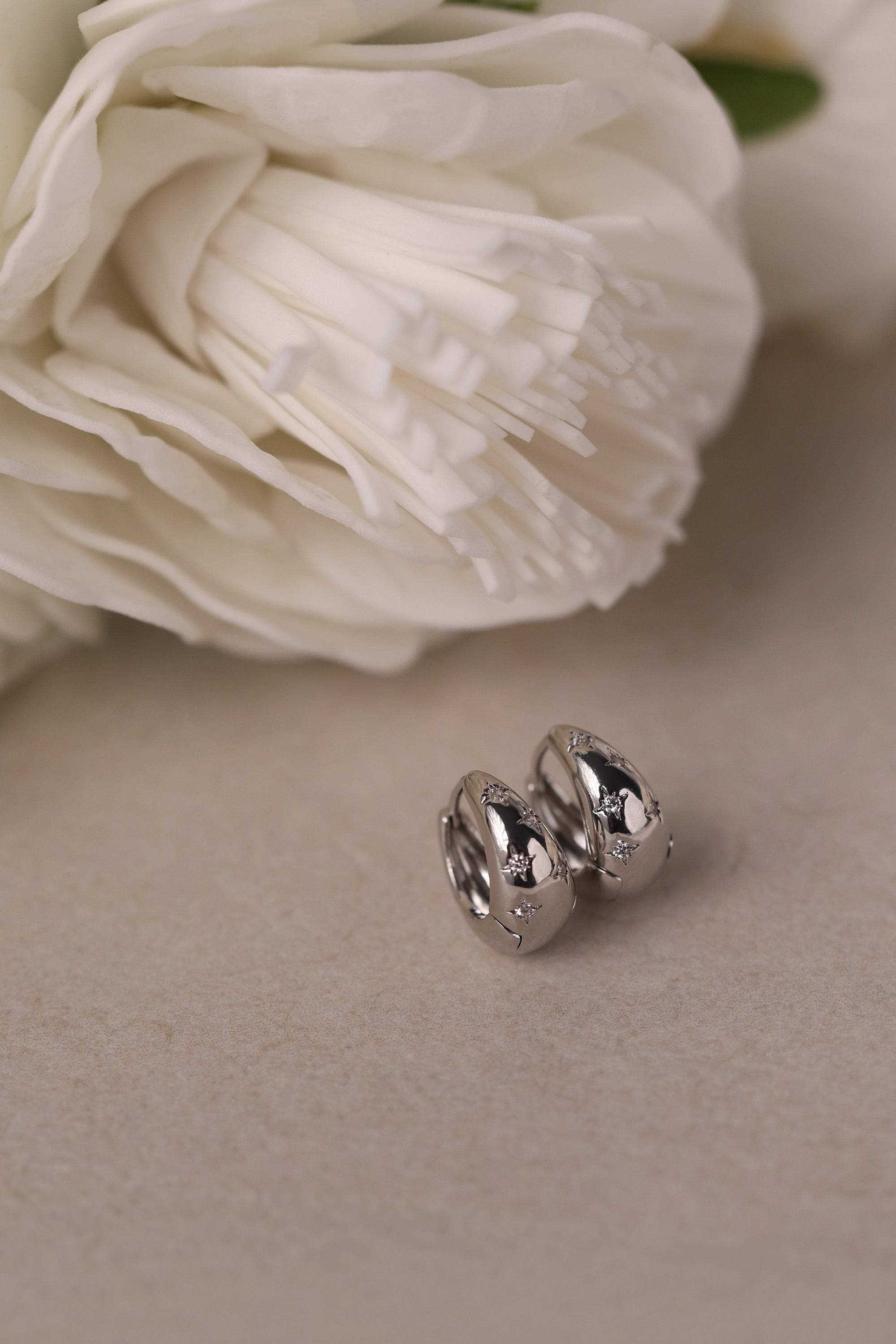 Gleaming silver hoop earrings with delicate star‑shaped engravings along the surface, reflecting light for a subtle sparkle; lightweight design shown in close‑up on a plain background.