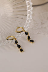 Gold hoop earrings with dangling teardrop gemstones in assorted colors, displayed on embroidered white lace