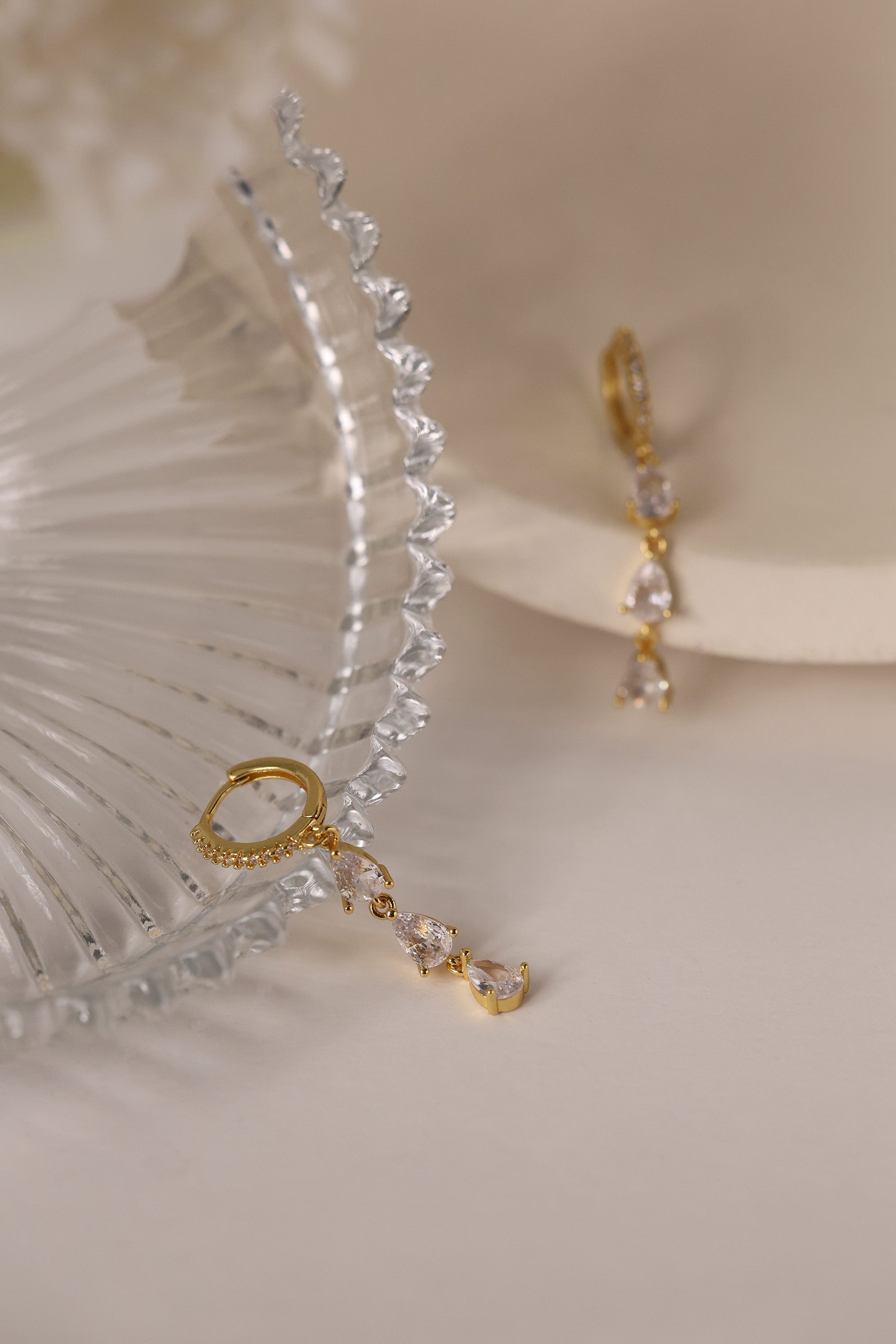 Gold hoop earrings with dangling teardrop gemstones in assorted colors, displayed on embroidered white lace