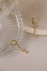 Gold hoop earrings with dangling teardrop gemstones in assorted colors, displayed on embroidered white lace