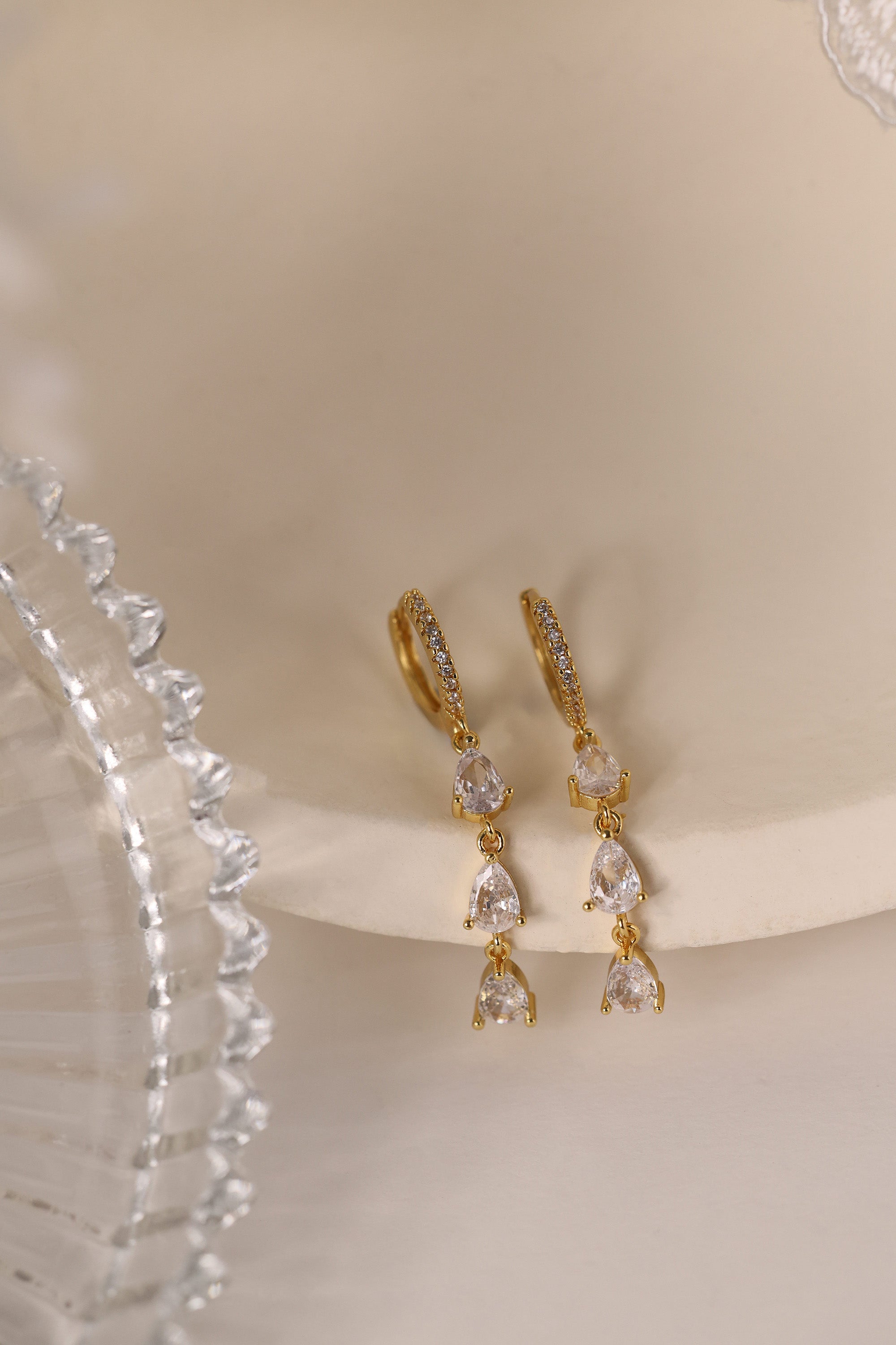 Gold hoop earrings with dangling teardrop gemstones in assorted colors, displayed on embroidered white lace