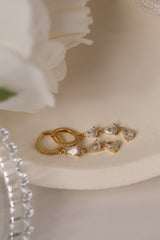 Gold hoop earrings with dangling teardrop gemstones in assorted colors, displayed on embroidered white lace