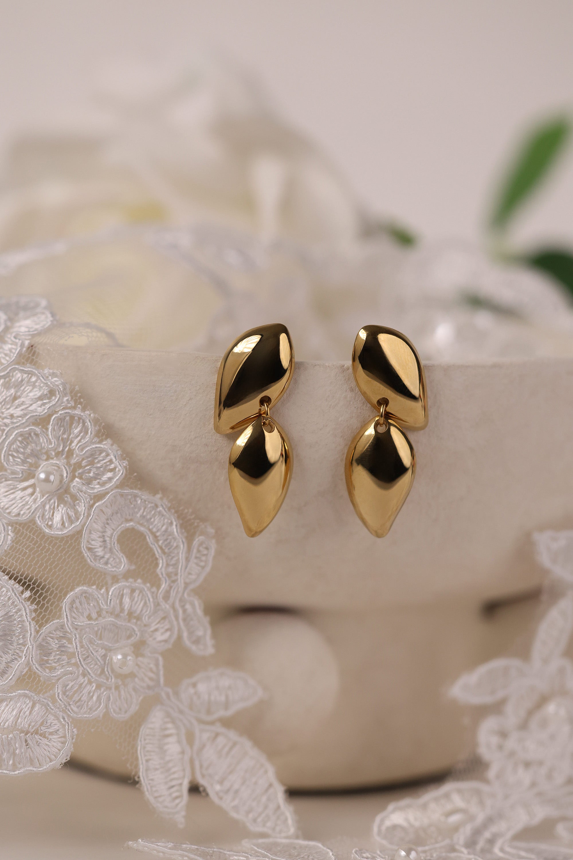 Gold stainless steel stud drop earrings with a polished teardrop design on a lace background.