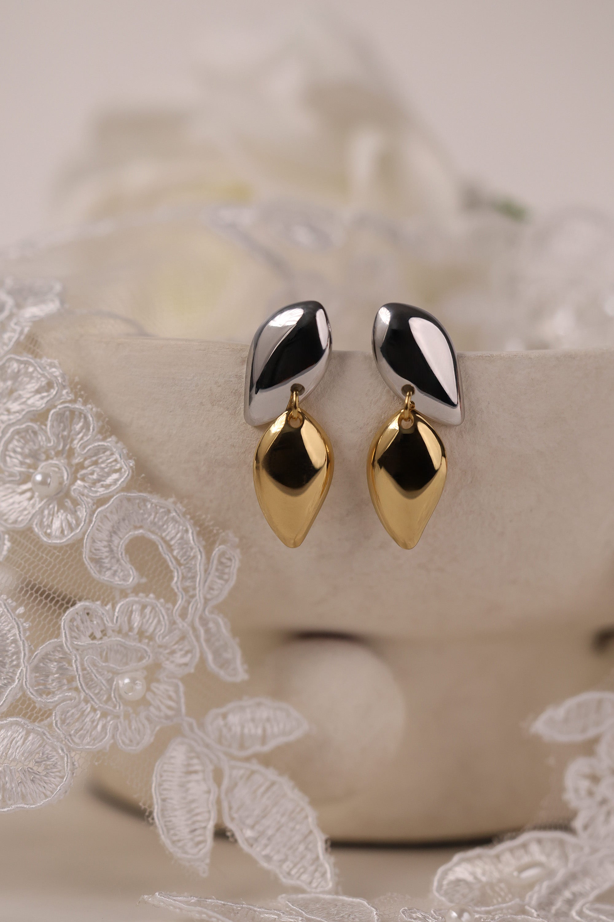 Two‑tone gold and silver stainless steel stud drop earrings with a polished teardrop design on a lace background.
