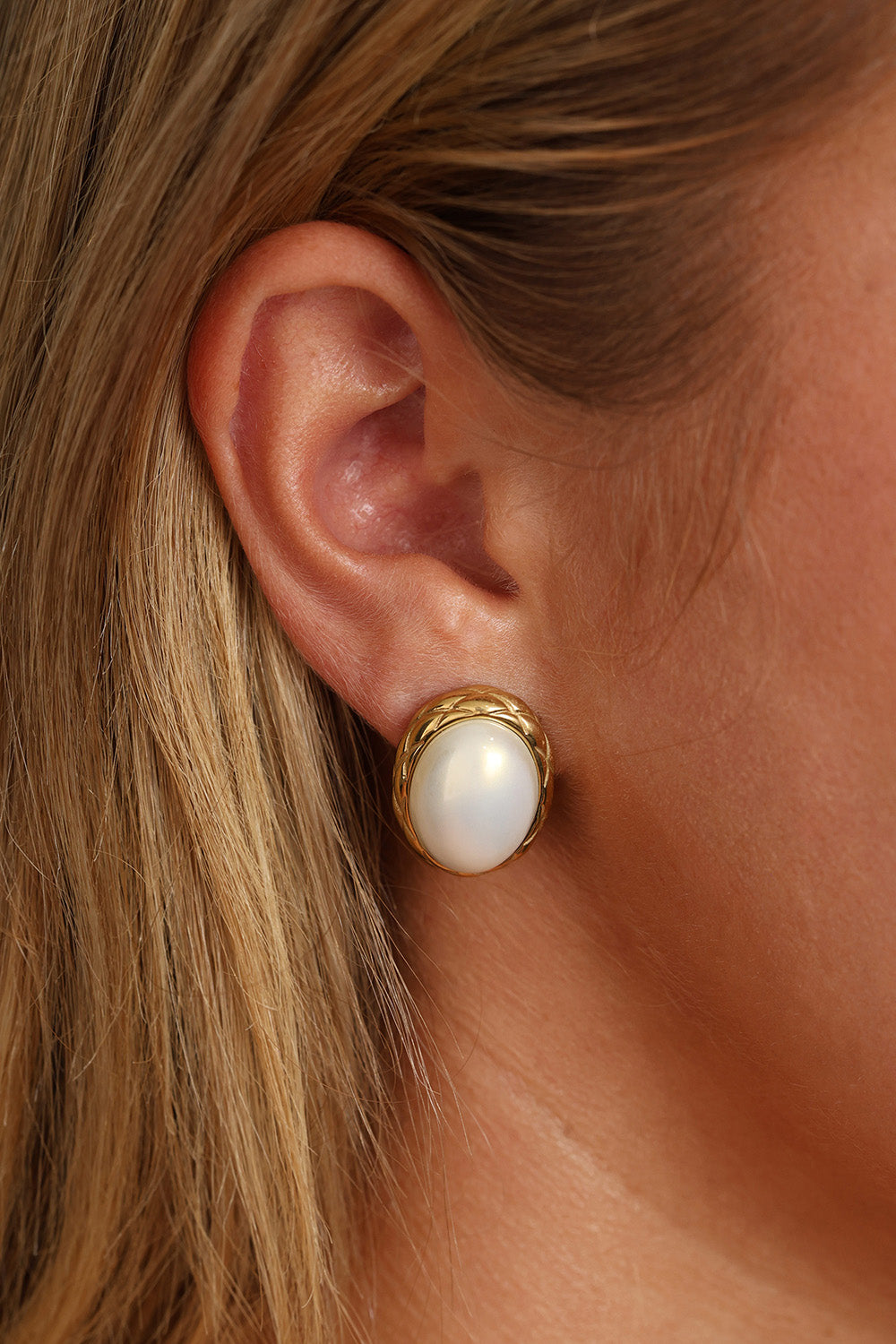 Gold stainless steel oval pearl stud earrings displayed on a glass dish with lace detail.