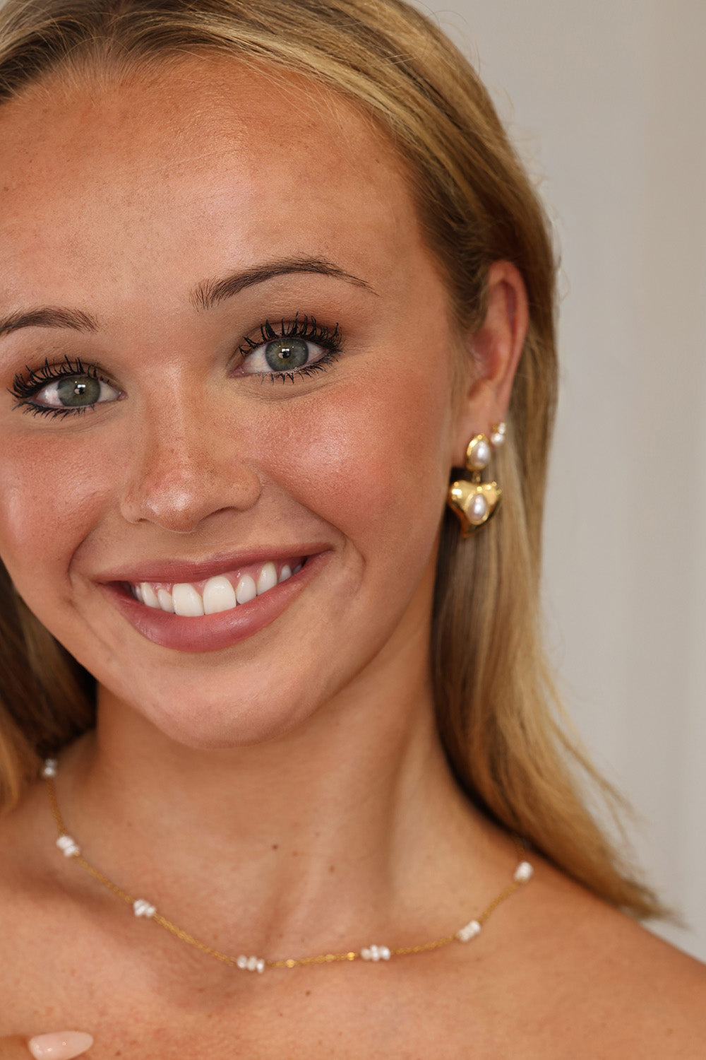 Gold heart stud drop earrings with teardrop pearls displayed on a soft lace background.