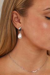 Stainless steel stud drop earrings with a large teardrop pearl worn on the ear.