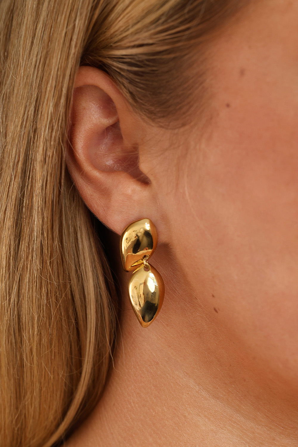 Gold stainless steel stud drop earrings with a polished teardrop design on a lace background.