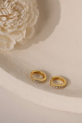 Pair of Sara 7mm pave huggie hoops in gold beside a cream flower