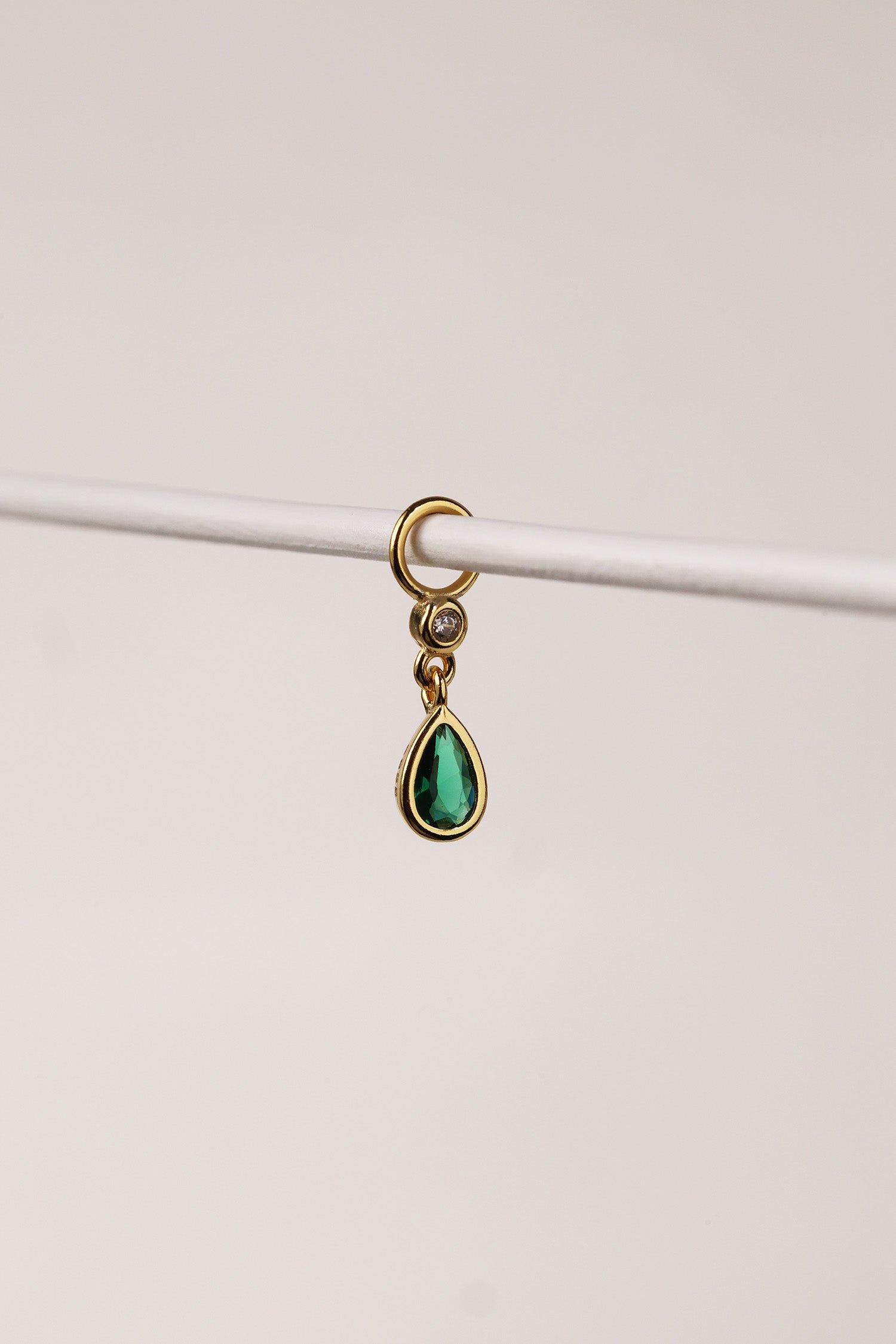 Gold teardrop bezel charm with emerald green gemstone hanging from a small hoop connector.