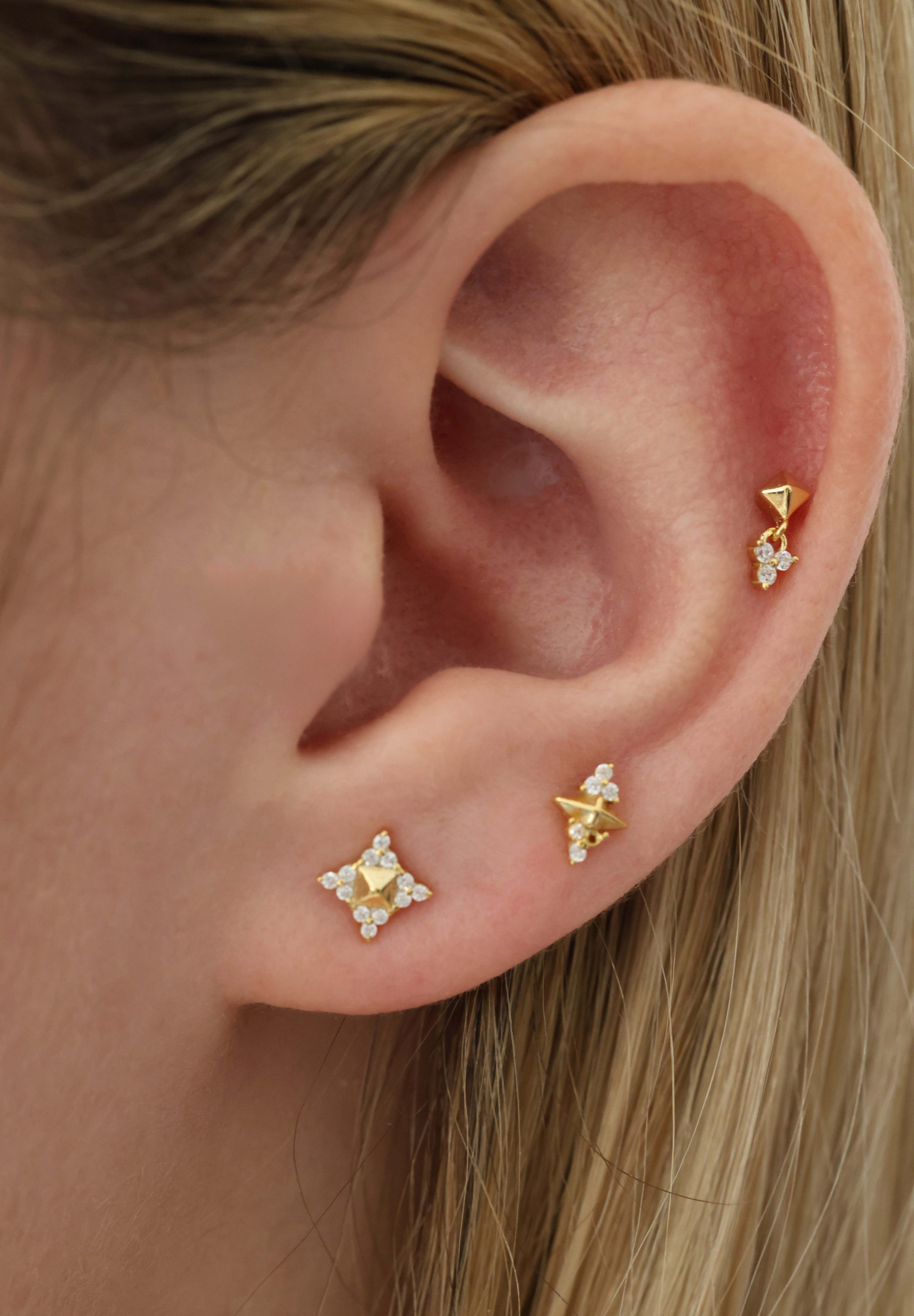 Close-up of a person's ear showcasing three gold ear piercings with small clear gemstone accents.