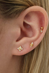 Close-up of a person's ear showcasing three gold ear piercings with small clear gemstone accents.
