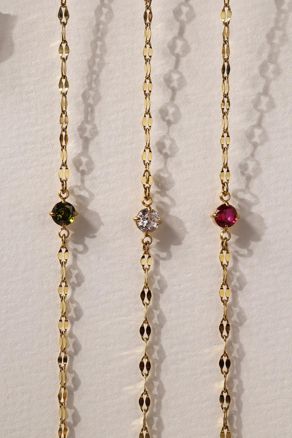 Gold stainless steel birthstone bracelet with a dainty chain and a single bezel‑set gemstone charm hanging at the centre.