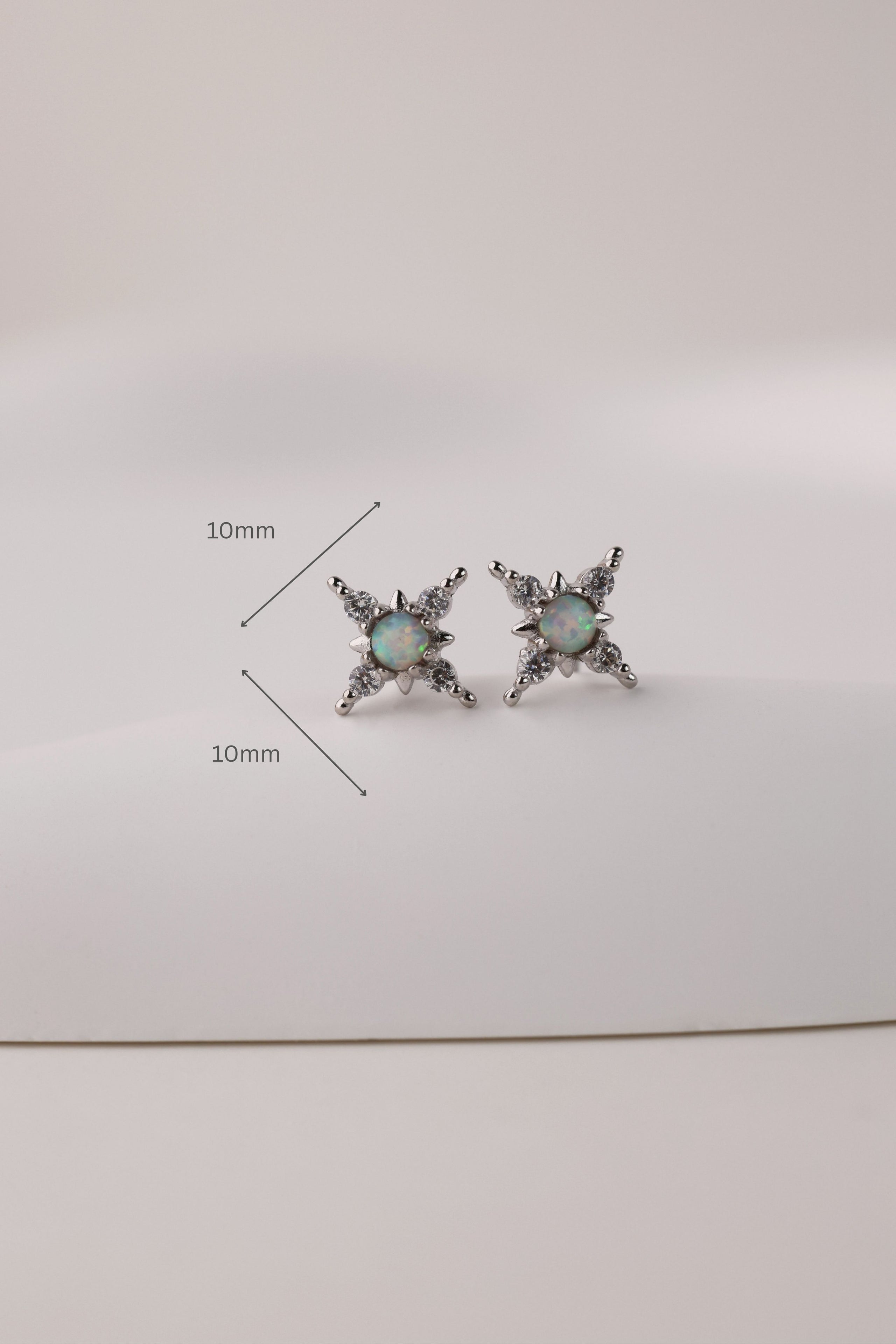 A pair of silver-toned starburst stud earrings with iridescent green-blue opal centers, shown on a plain light background with 10mm size measurement lines overlaid.
