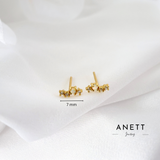 A pair of small gold stud earrings with clustered crystal-like details, shown on a soft white fabric background with a 7 mm size marker and the brand name ANETT Jewelry.