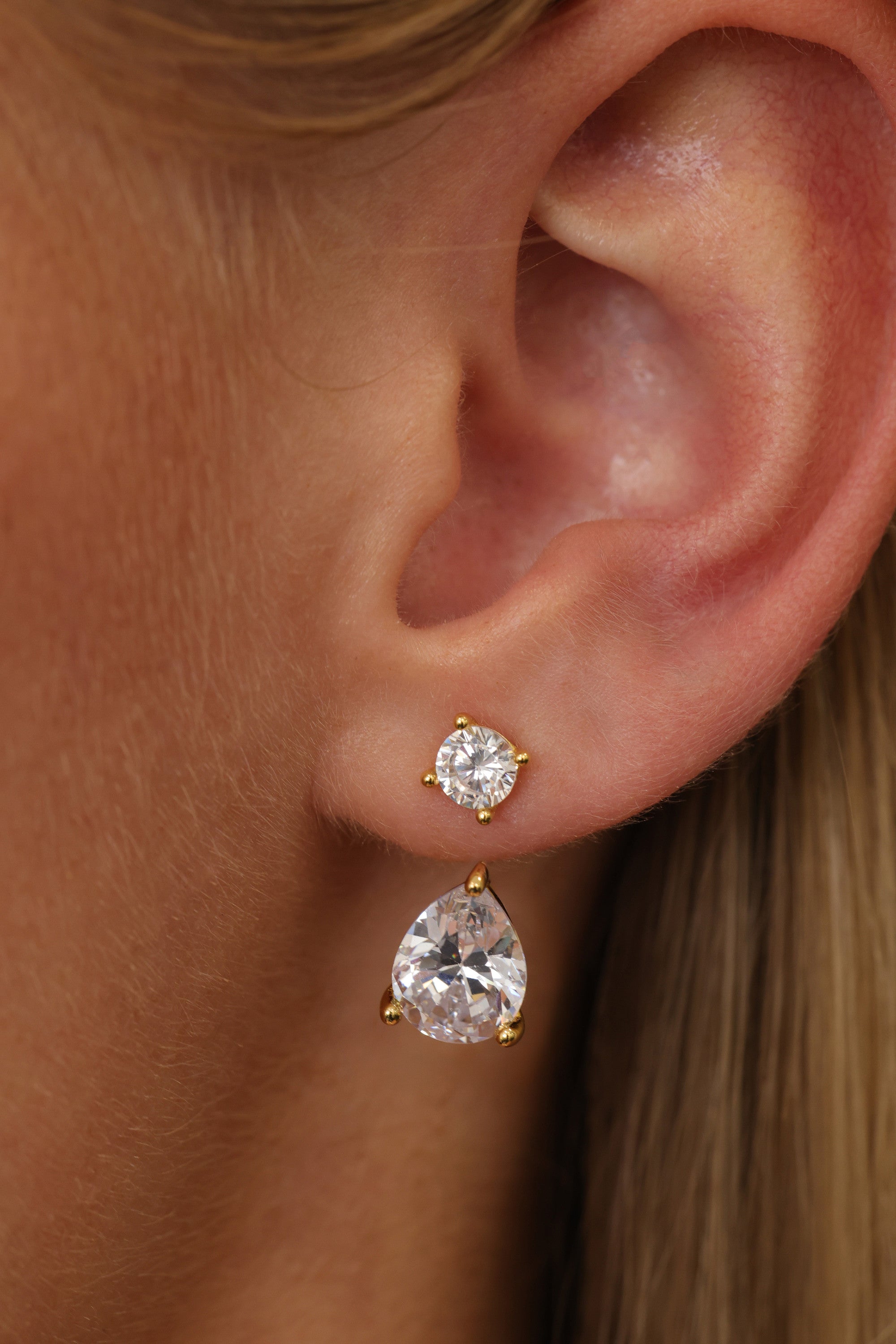 Close-up of the gold Adamas ear jacket on an ear — round stud above a 2 carat pear-cut cubic zirconia drop.