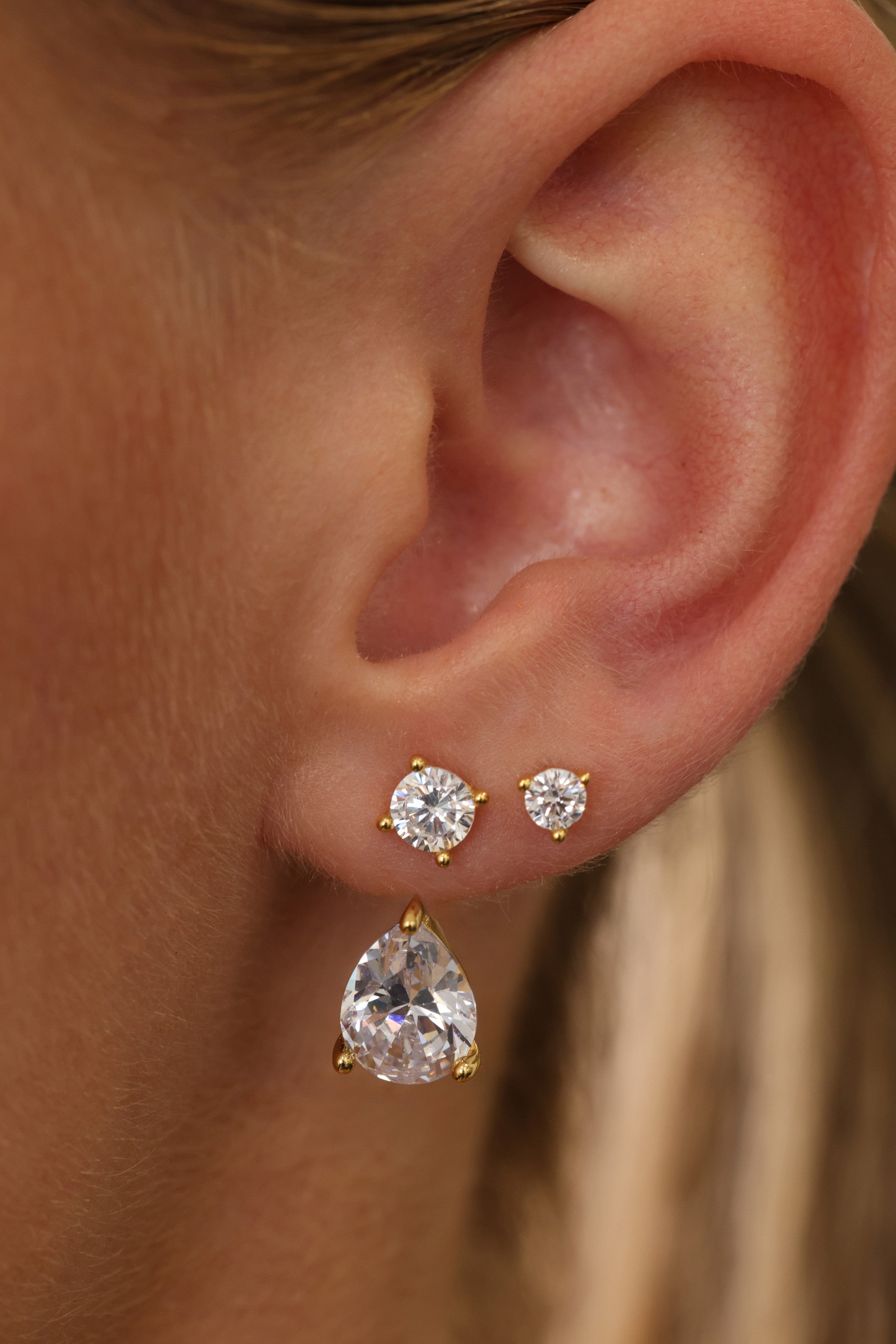 Gold Adamas ear stack close-up — two round cubic zirconia studs with the pear-cut drop below them.