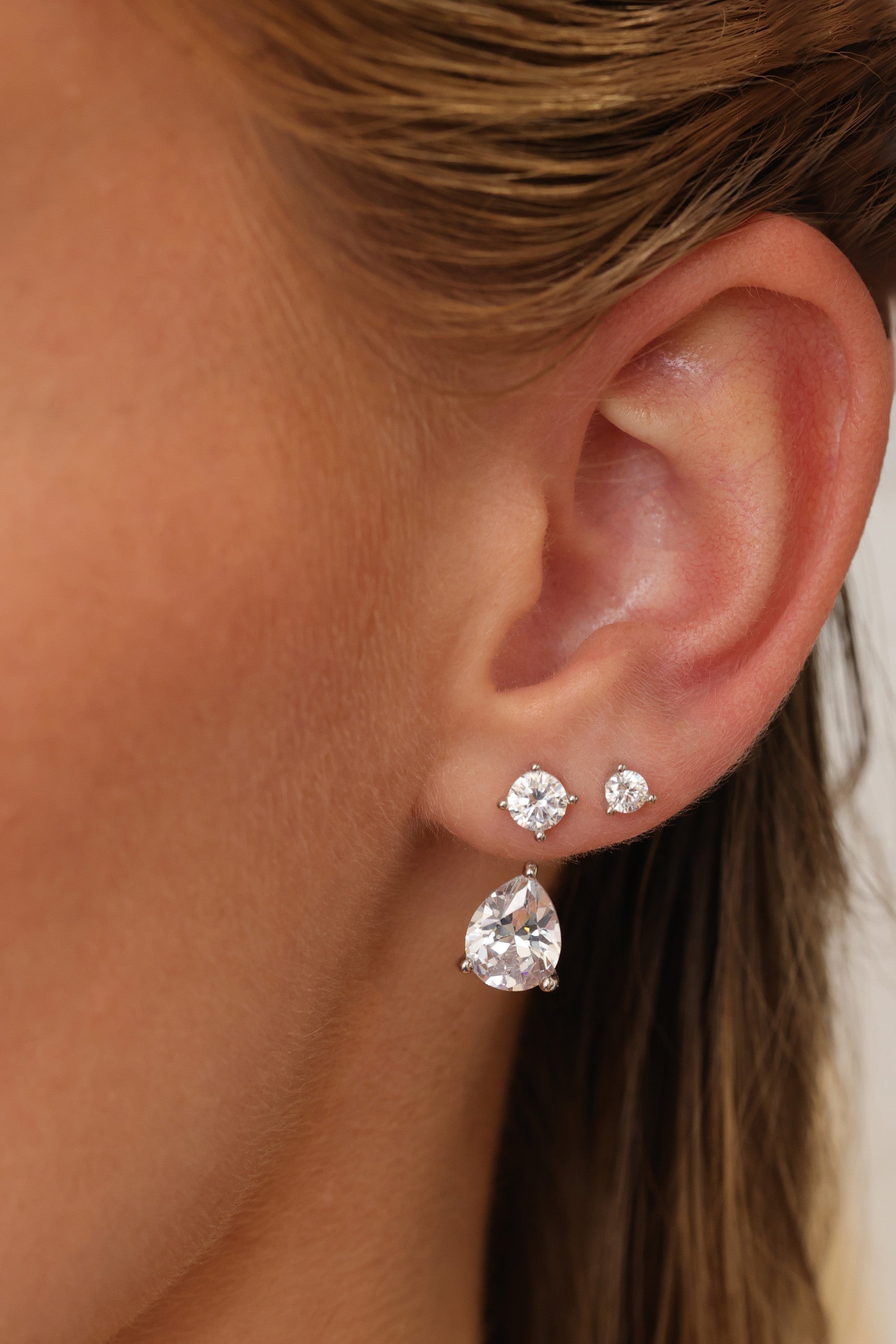 Silver Adamas ear jacket worn with two round cubic zirconia studs above the pear-cut drop on one lobe.