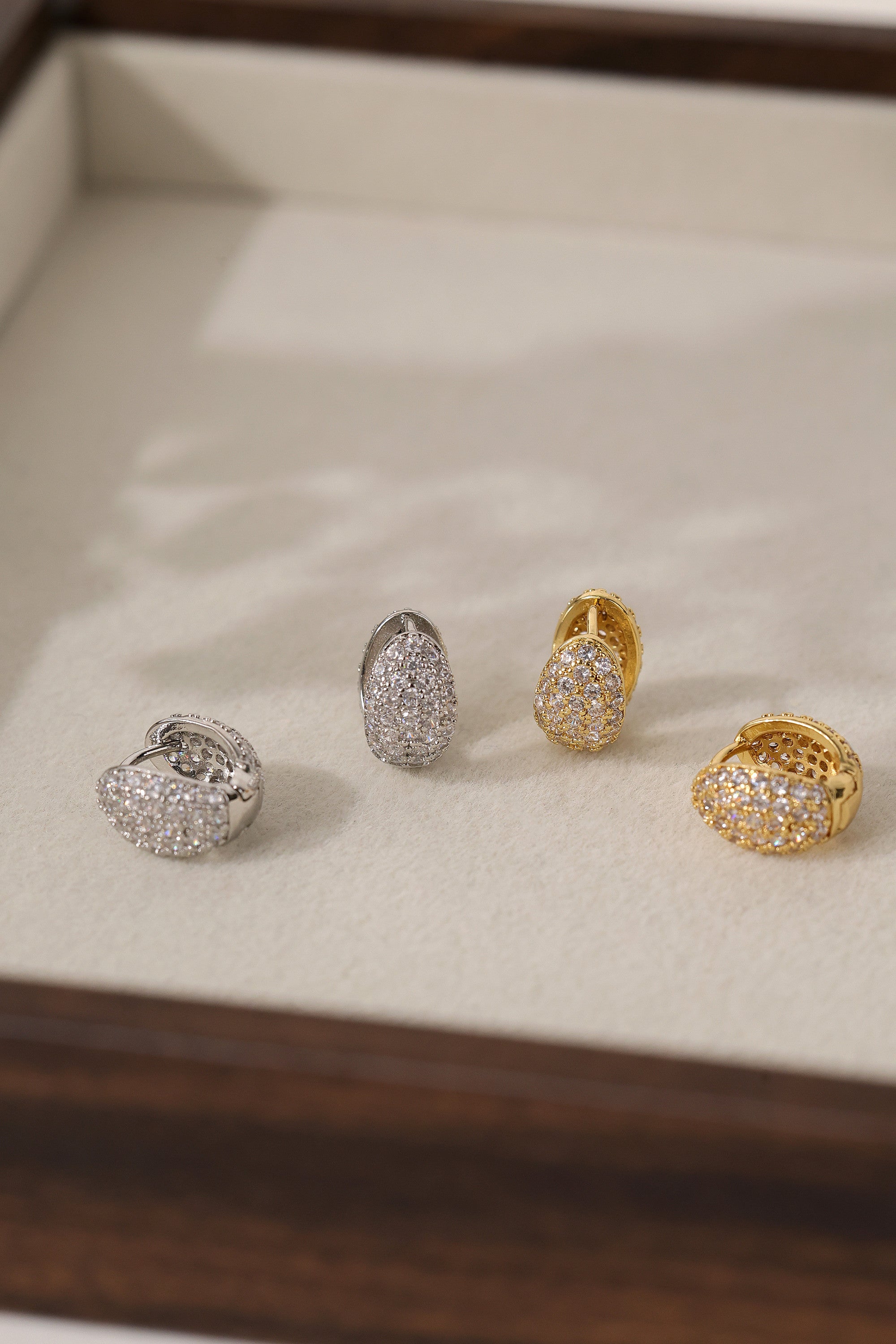 Cleo Pavé huggie hoops in gold and silver side by side in a tray, showing both metal finishes.