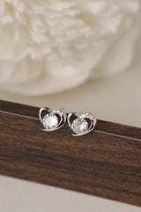Close-up of sterling silver open heart stud earrings with a sparkling round CZ stone, displayed on a dark wooden stand