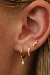 Gold opal dangle huggie worn with a pavé cubic zirconia huggie and an opal stud in a three-piece ear stack.