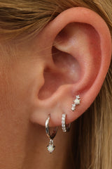 Silver opal dangle huggie worn with a pavé cubic zirconia huggie and an opal stud in a three-piece ear stack.