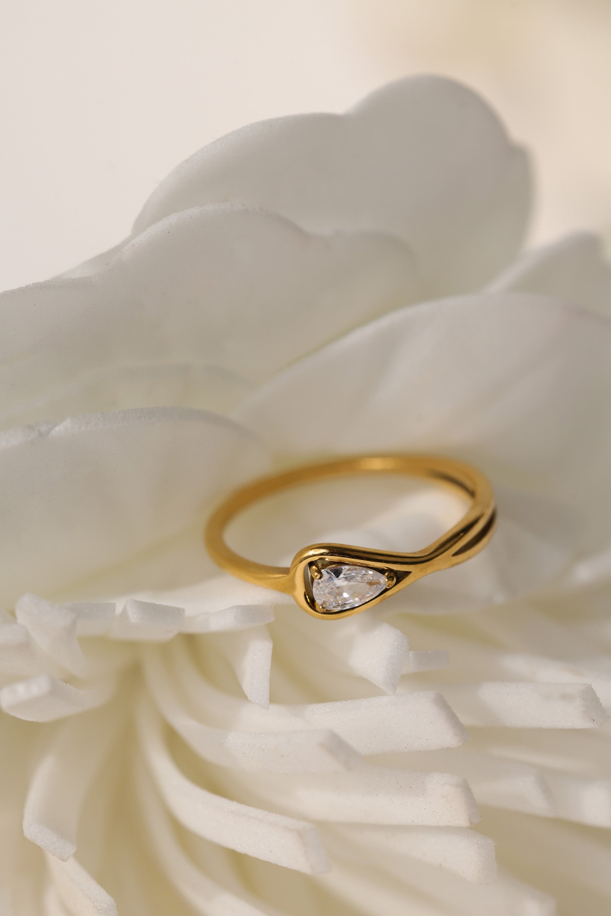 Eloise pear solitaire ring in gold beside a white flower