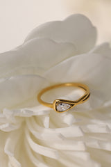 Eloise pear solitaire ring in gold beside a white flower