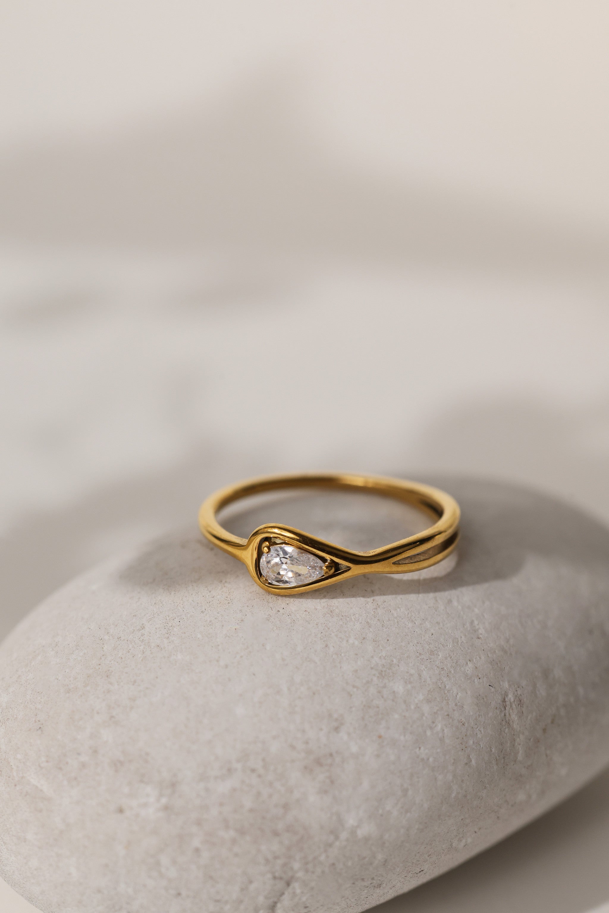 Eloise pear solitaire ring in gold resting on a pale stone